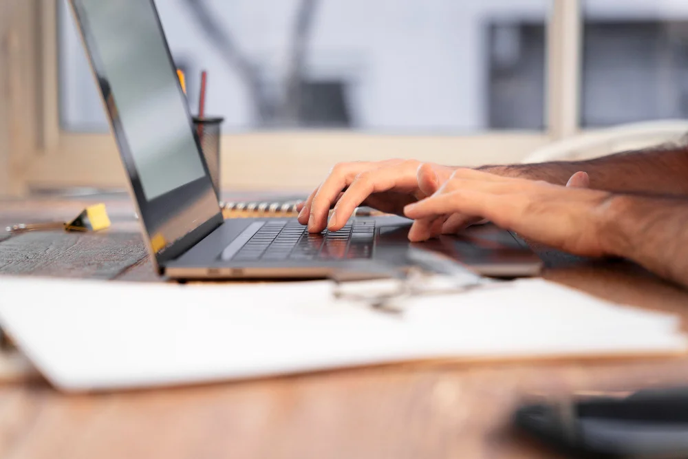 homem digitando com papéis espalhados na mesa