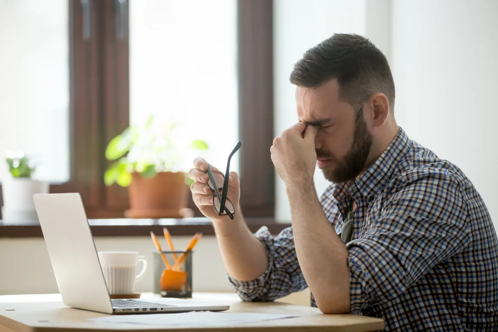 cansaço mental: homem cansado com a mão nos olhos em frente ao notebook